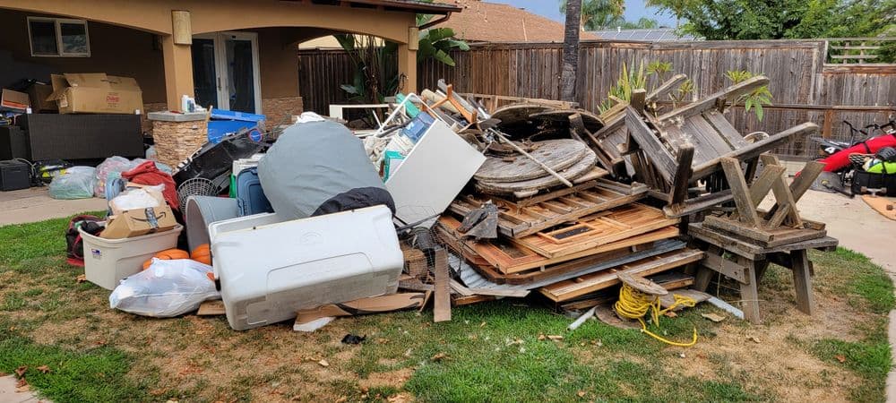 Pile of clutter including furniture and debris in a backyard setting.