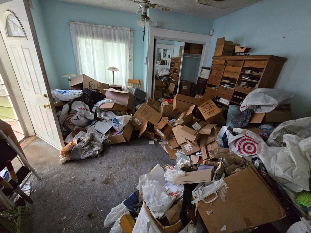 Cluttered room filled with cardboard boxes and trash, showing disorganization and neglect.