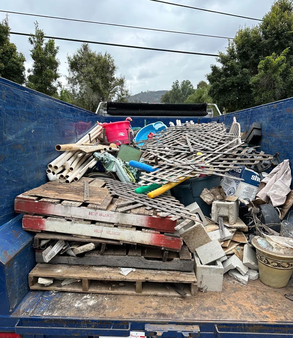 Dump truck filled with assorted construction debris, pallets, and tools for disposal.