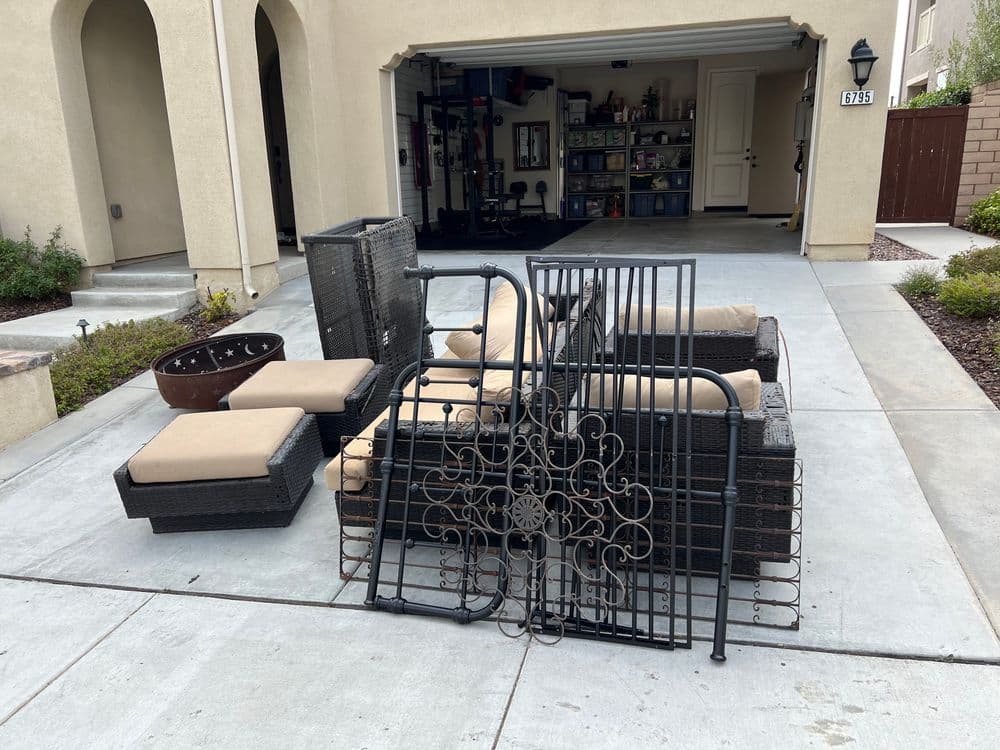 Outdoor furniture set with cushions and a metal decorative gate, arranged in a driveway.