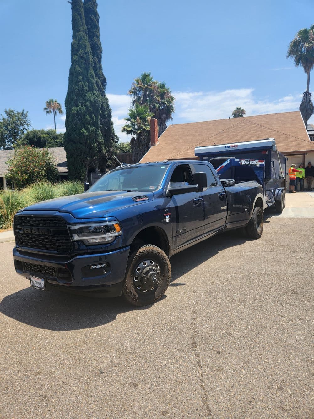 Blue pickup truck parked in front of a house with palm trees and a trailer.
