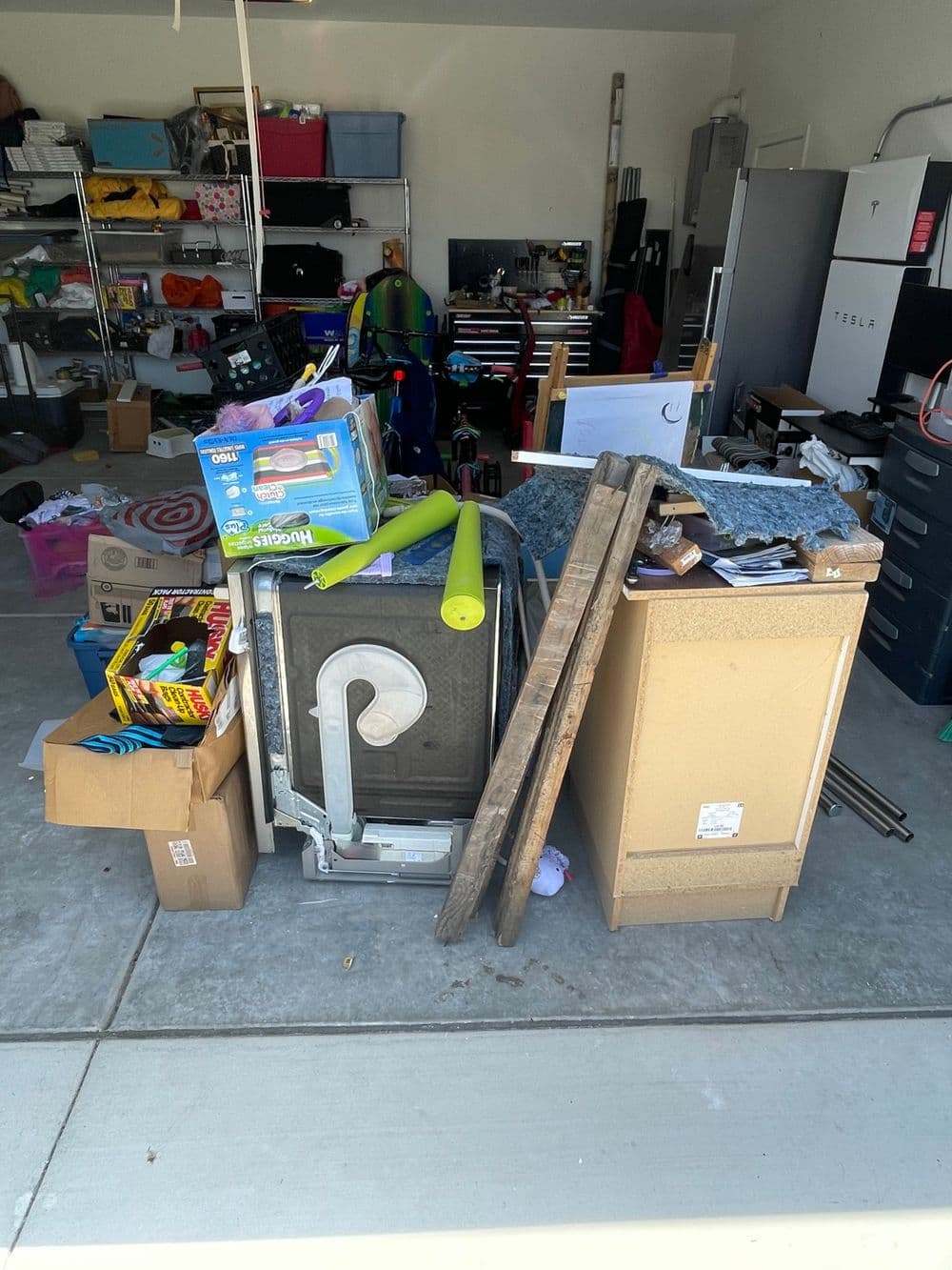 Cluttered garage filled with boxes, toys, tools, and a washing machine.
