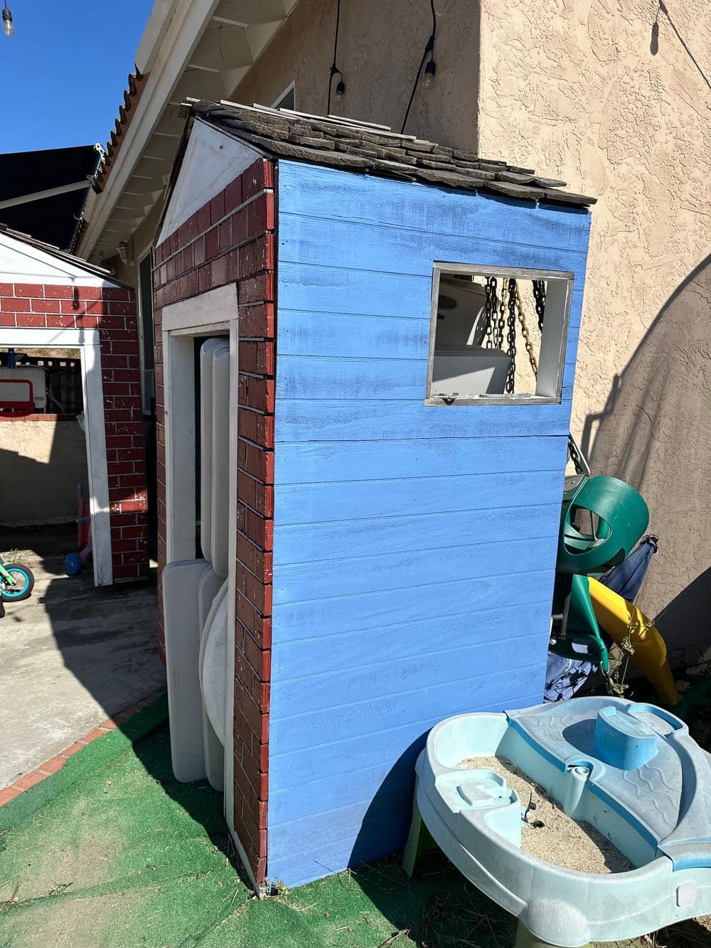 Colorful playhouse with blue siding and brick accents in a backyard setting.