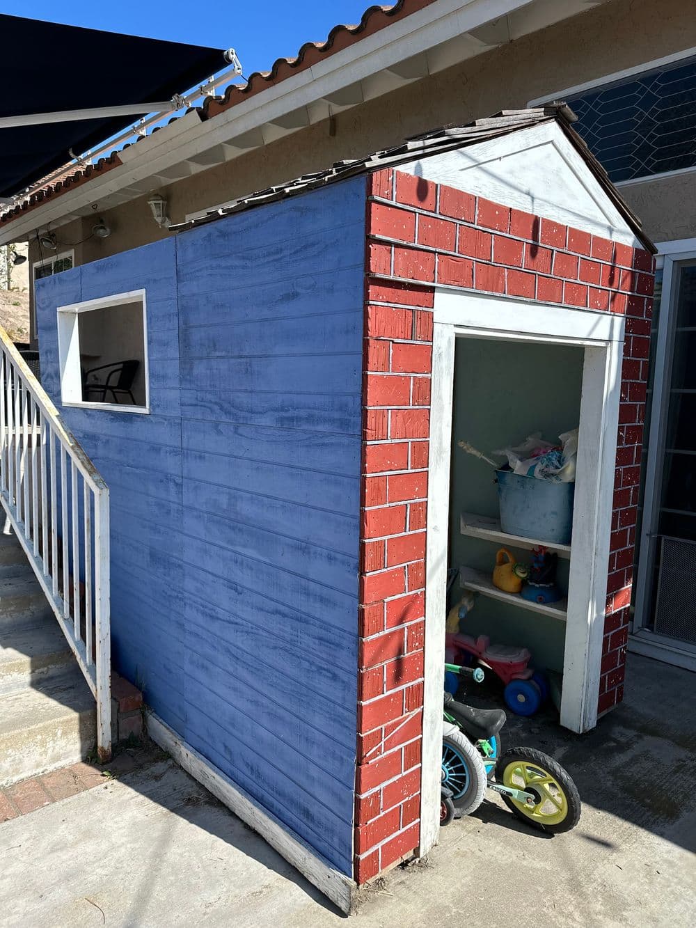 Colorful outdoor playhouse with blue walls and red brick accents next to a house.