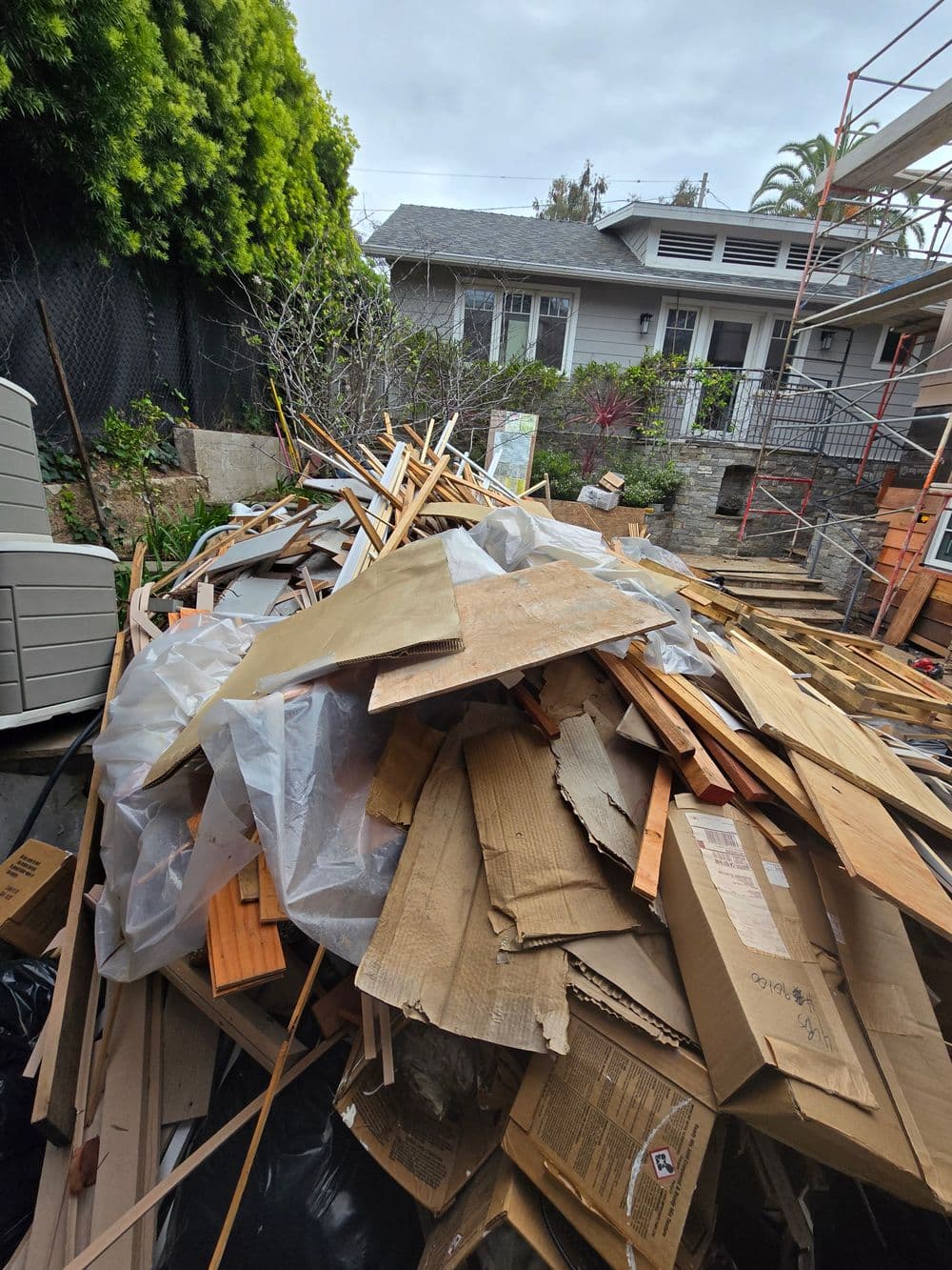 Pile of construction debris including wood, cardboard, and plastic in a residential area.