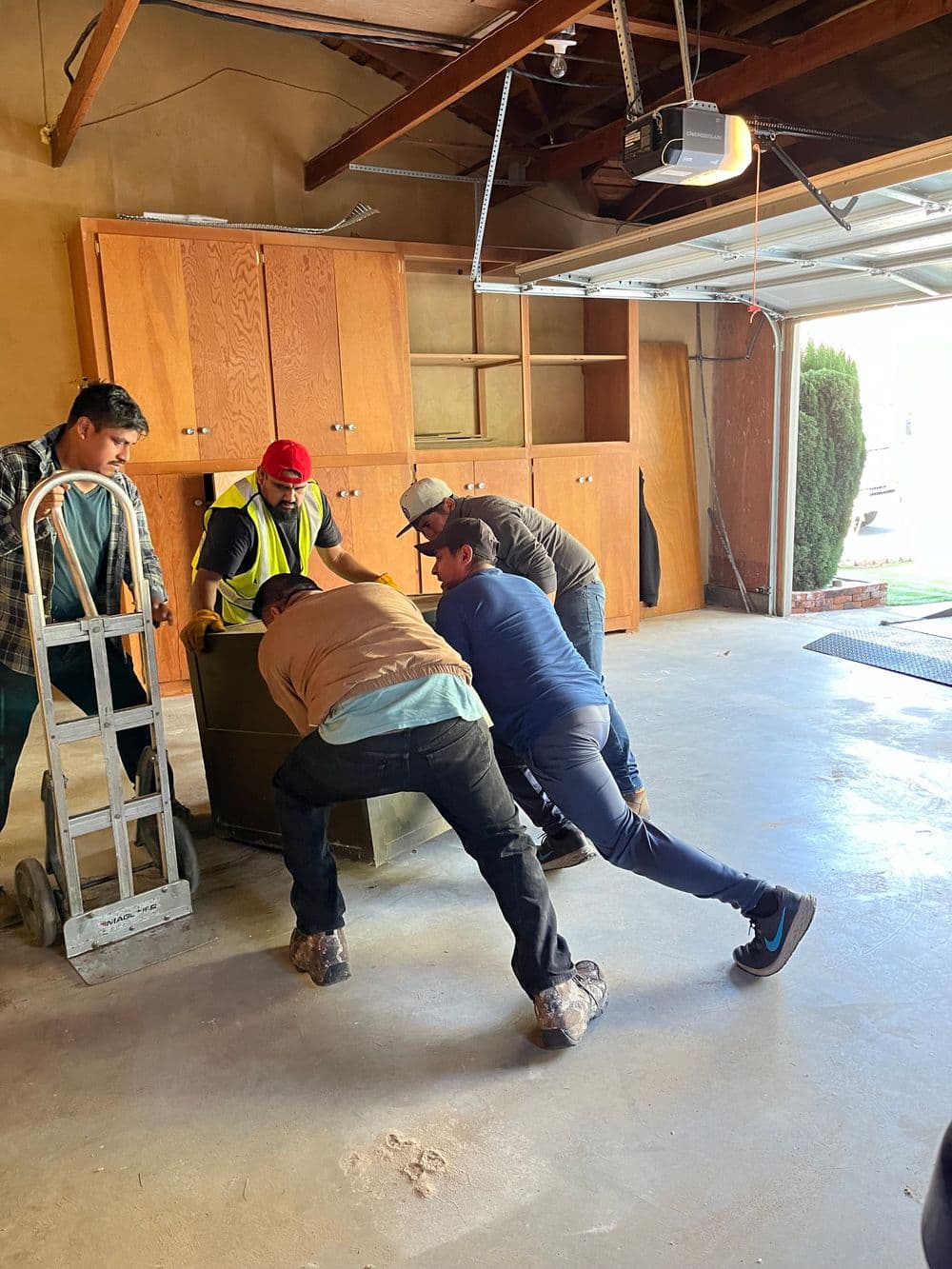 Group of five men lifting a heavy object in a garage with wooden storage cabinets.