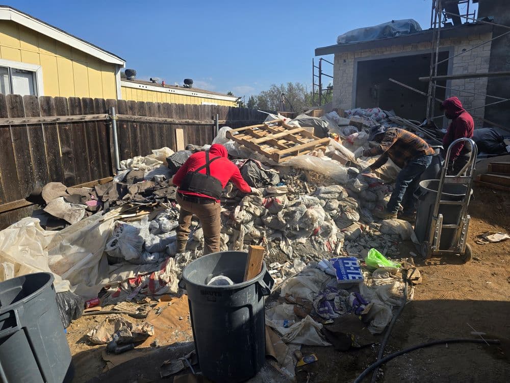 Workers sifting through a large pile of debris and trash in a construction site.