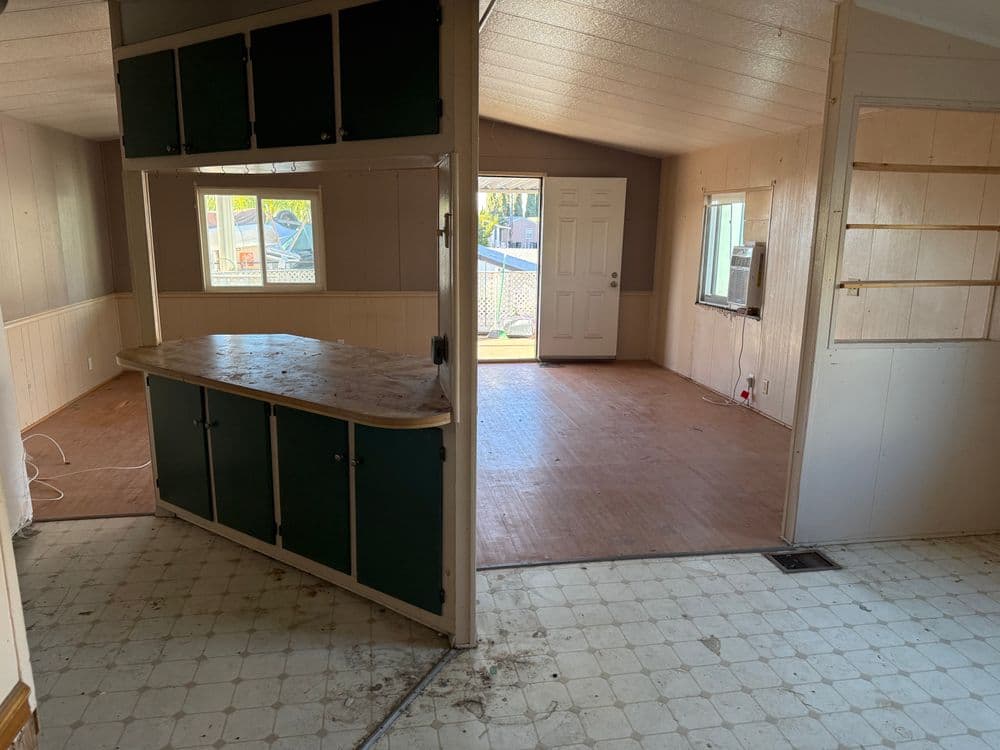 Renovated interior showing open kitchen and living area with large windows and wood flooring.