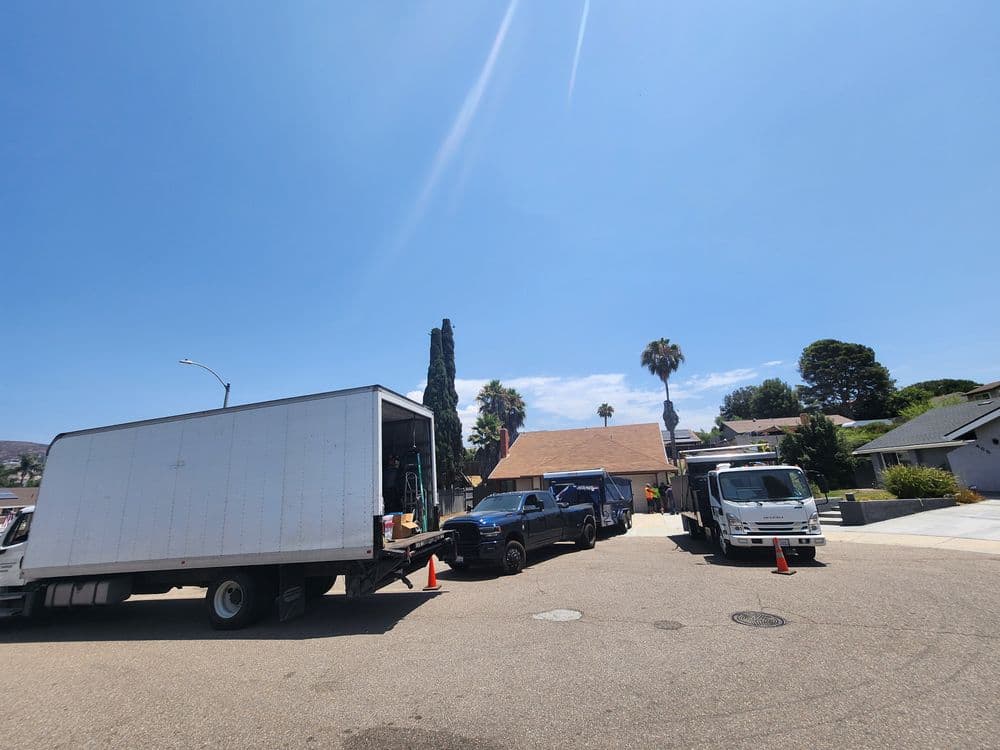 Moving trucks parked on a residential street with palm trees and blue sky in the background.
