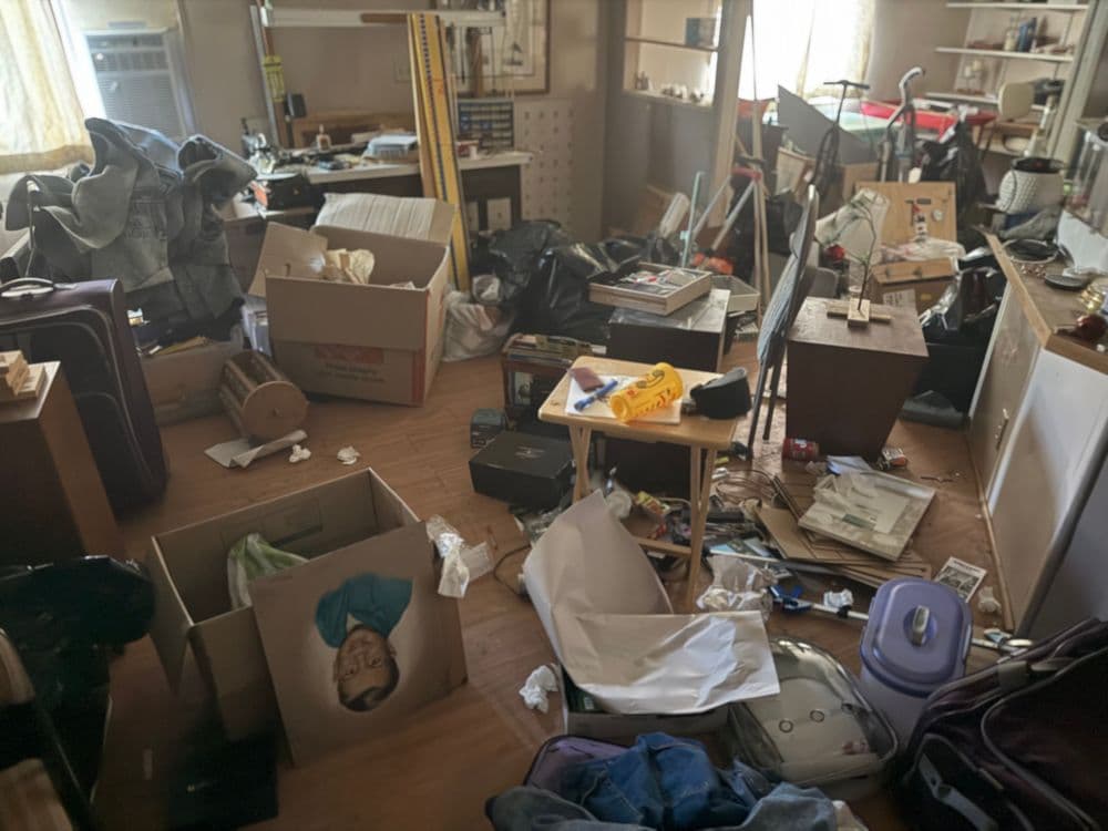 Cluttered room filled with boxes, bags, and scattered belongings. Disorganized and chaotic space.