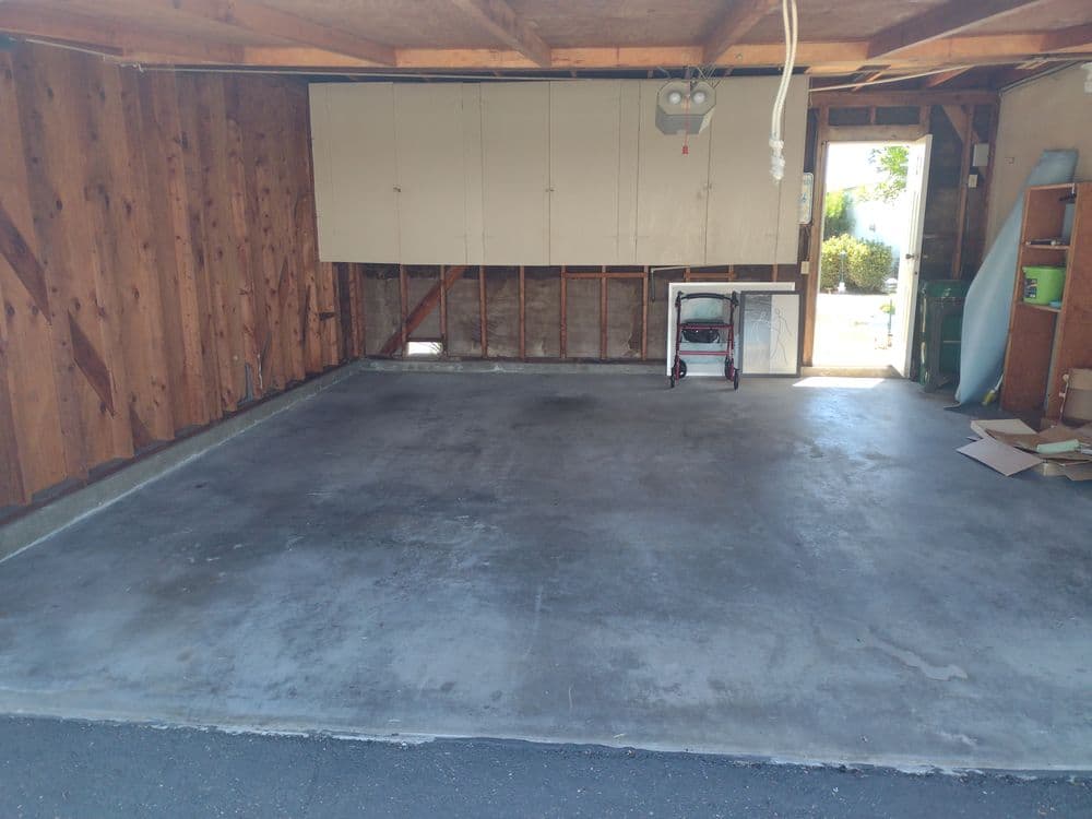Empty garage with wooden walls and a concrete floor, featuring a storage area and natural light.