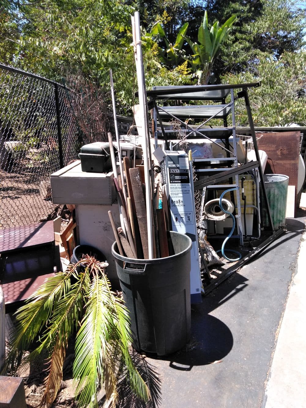 Cluttered outdoor space with discarded items, a trash can, and mixed debris.